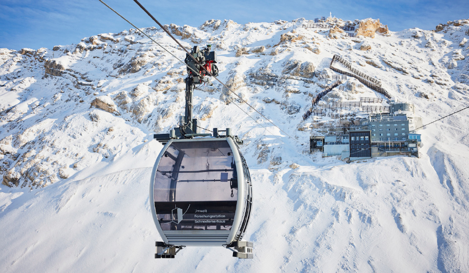 A cable car travelling up a large, snow-covered mountain 