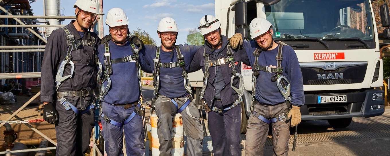 Five scaffolders wearing personal protective equipment standing in front of a scaffold, a XERVON vehicle in the background