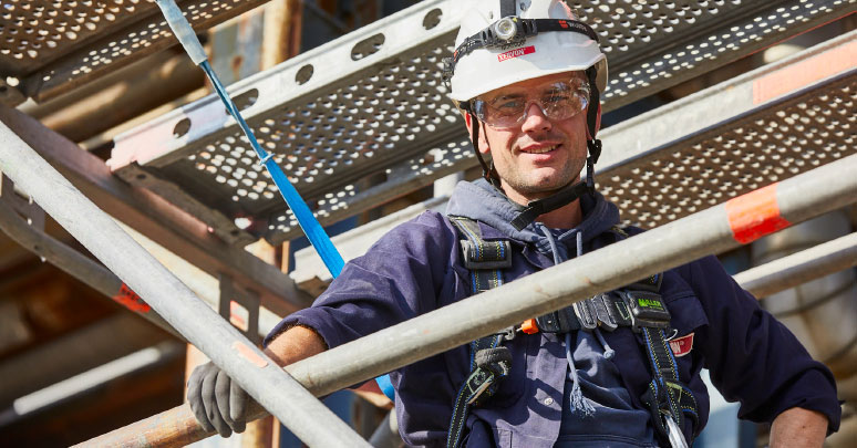 A scaffolder wearing personal protective equipment and a safety harness standing on a scaffold